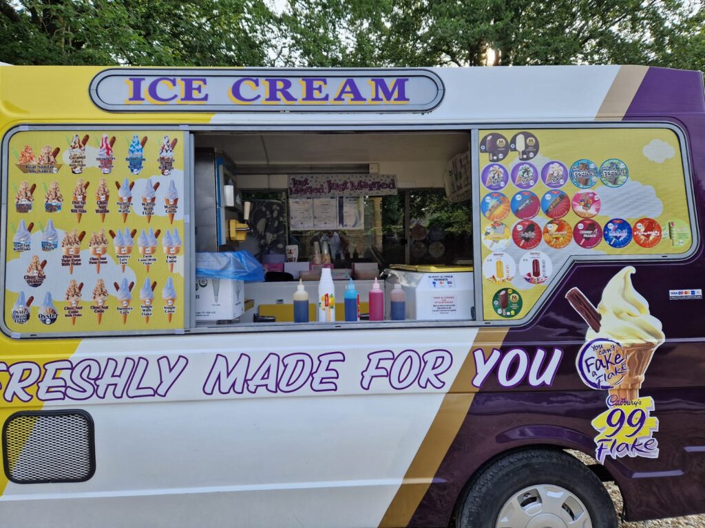 Side view of Lollie Dollies ice cream van serving customers in Woking, with a colourful menu of sweet treats and cold desserts.